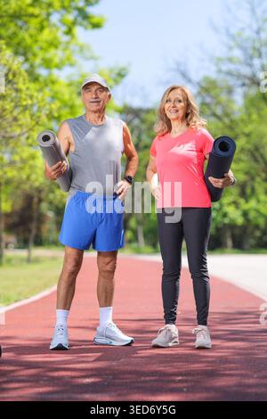 Elderly couple with exercise mats posing in a park Stock Photo