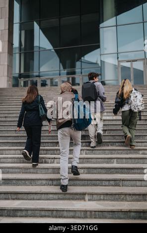 High school students walking up steps toward a modern school building with backpacks and books Stock Photo