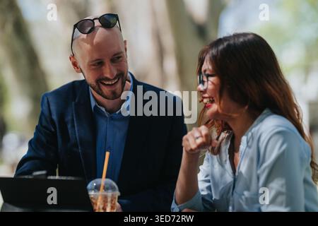 Business colleagues smiling and chatting during outdoor meeting at a cafe with laptop Stock Photo
