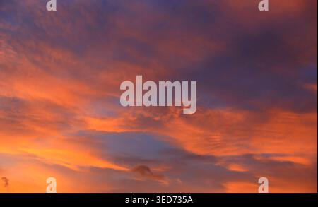 The sky is painted with a breathtaking blend of fiery orange and deep purple hues as the sun sets, casting dramatic shadows and highlights across the Stock Photo