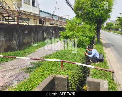 person using surveying equipment in a drainage ditch, surveying transit,  used to measure angles, distances for construction. HCMC, Vietnam Stock Photo