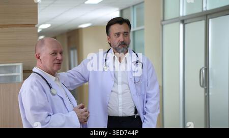 Doctors discuss. Two experienced doctors discussing patient information and medical reports in a hospital corridor. Professional healthcare teamwork c Stock Photo