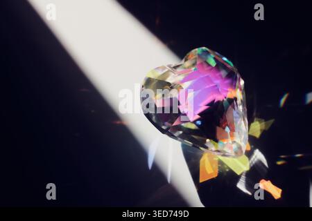 Crystal heart scatters light, creating vibrant colors and shimmering reflections on dark background Stock Photo
