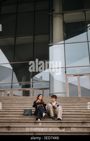 High school students studying and talking on campus steps outside a modern school building Stock Photo