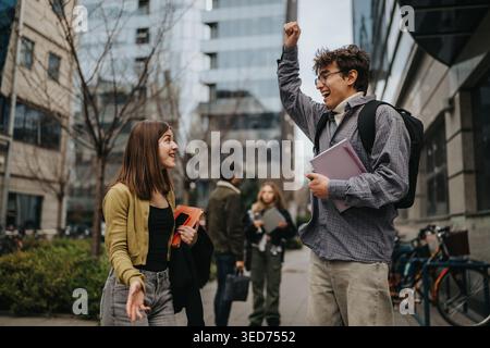 Students celebrating and talking on an urban campus walkway with backpacks and notebooks Stock Photo