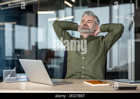 Mature businessman finding a moment of calm and peace, leaning back in his office chair with hands behind his head and eyes closed, taking a refreshing break from a busy workday Stock Photo