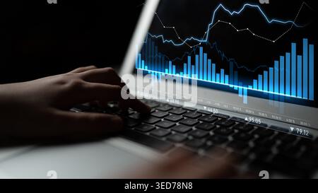 A person is working on a laptop, actively engaging with financial charts and graphs in a dark setting, highlighting the significance of data analysis Stock Photo