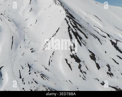 Aerial view of the snow-covered slopes of Mount Etna south side with ski lift pylons and dark volcanic rock patches in Nicolosi, Sicilia, Italy. Stock Photo