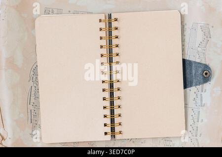Flat lay of open notebook with spiral binding lies on sheet music, with blank pages ready for notebook layout, writing, journaling, study, or planner Stock Photo