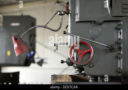 Close up of industrial milling machine shows red handwheel, control lever and flexible work lamp on heavy metal body with visible wear and oil traces. Stock Photo