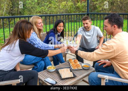 Happy friends toasting drinks celebrating together and enjoying snacks outdoors on a patio Stock Photo