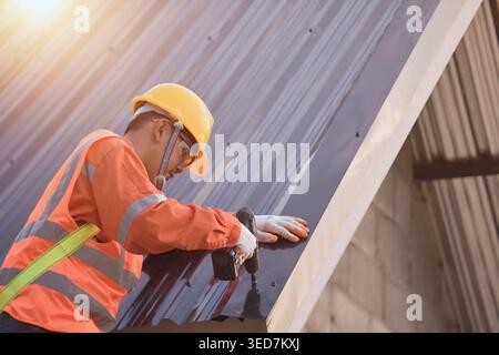 Side view of a Construction worker installing metal sheets on a roof, Thailand Stock Photo