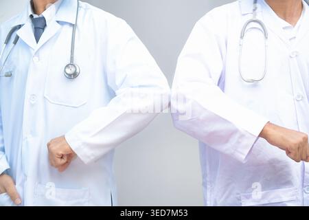 Close-up of two doctors in laboratory coats and stethoscopes greeting each other by bumping elbows Stock Photo