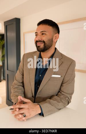 Portrait of a smiling businessman in a suit standing next to a high-top table looking sideways Stock Photo