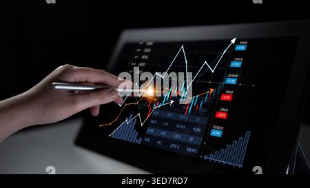 A close-up of a hand using a stylus on a digital screen, displaying stock market graphs and data visualization for professional financial analysis and Stock Photo