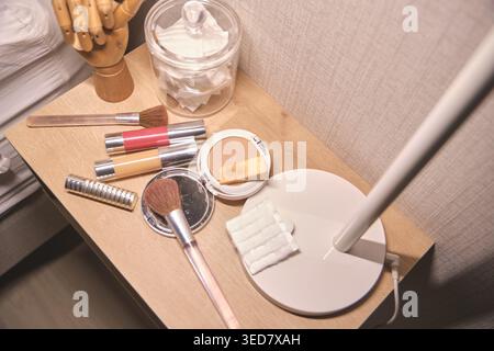 Makeup brushes, compact powder, and skincare items on a wooden vanity table Stock Photo