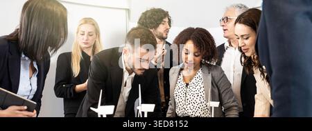 Multicultural team of engineers and business professionals discussing wind turbine models and renewable energy strategy in modern office meeting. Mill Stock Photo