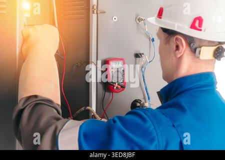 An electrician uses a multimeter to test electrical circuits in a control panel. The setting is professional and technical, showcasing precision work. Stock Photo