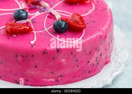 Homemade mousse cake with pitahaya and fresh berries. Decorated with blueberries, raspberries, flower petals and white chocolate on a light background Stock Photo