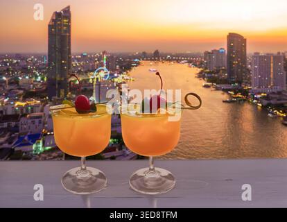 Two tropical cocktails on a rooftop in Bangkok overlooking a the River at sunset Stock Photo