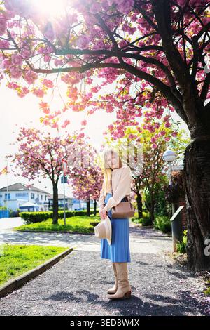 Woman posing beneath pink blossoms, romantic spring atmosphere and travel lifestyle vibe. Stock Photo