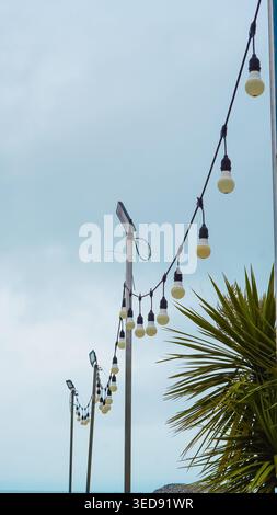 String of outdoor light bulbs hanging from poles against an overcast sky Stock Photo