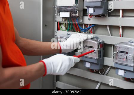 Electrician with screwdriver checking electrical meter indoors, closeup Stock Photo