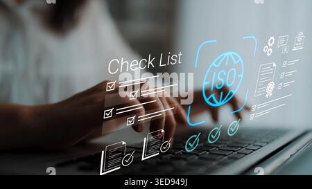 Hands typing on laptop keyboard with digital check list and ISO symbol displayed on screen in modern workplace setting emphasizing organization and Stock Photo