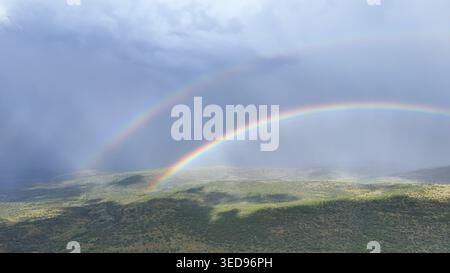 Aerial view of a double rainbow arching over the green hills and valleys of the Waterberg region under a dramatic stormy sky Waterberg District Munici Stock Photo