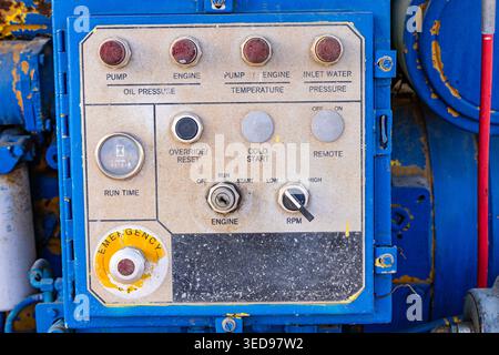 Close up of a weathered industrial control panel with emergency stop button and gauges on blue heavy machinery Stock Photo