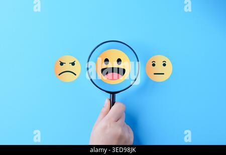 Customer satisfaction survey and positive feedback concept. hand holding magnifying glass over happy emoji, showing service quality, user experience, Stock Photo
