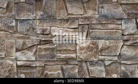 Wall decoration with square stone tiles of various sizes in grey-brown colour with a textured surface imitating the relief of natural stone is a decor Stock Photo