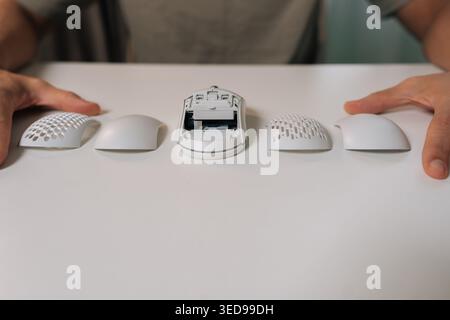 Close-up of person hands on white desk showing disassembled ergonomic wireless computer mouse with core unit and four interchangeable shells Stock Photo