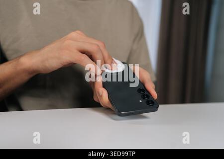 Close-up hands of man cleaning and disinfecting black smartphone with cotton pad, maintaining personal hygiene and device sanitation, preventing germ Stock Photo