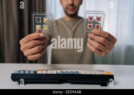 Man holding two packs of mechanical keyboard switches, comparing options for customizing or repairing a wireless mechanical keyboard on clean white Stock Photo