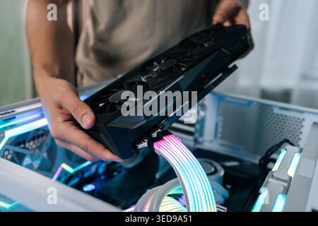 Person upgrading gaming computer, installing powerful graphics card into open pc case, showing internal components with rgb led lighting and custom Stock Photo