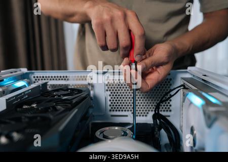 Close-up of technician hands maintaining and upgrading a personal computer, assembling internal hardware components with screwdriver, performing Stock Photo
