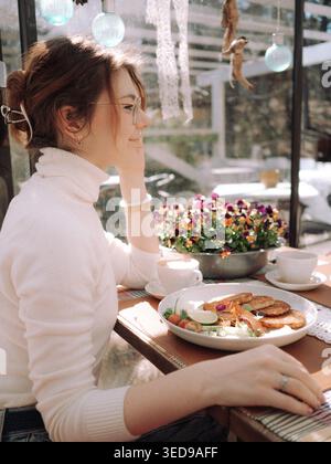 Young woman enjoying brunch at vintage cafe Ott and Matilda Kohvik in Tallinn, Estonia, on a sunny spring day Stock Photo