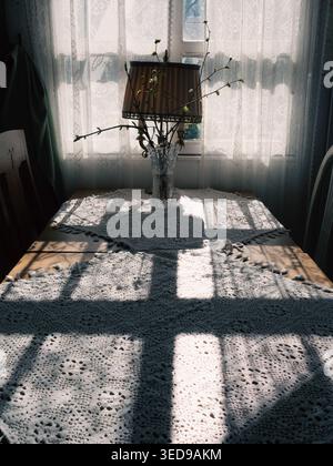Sunlight casting window shadows on a lace tablecloth with budding branches in a vase at Ott and Matilda cafe, Estonia Stock Photo