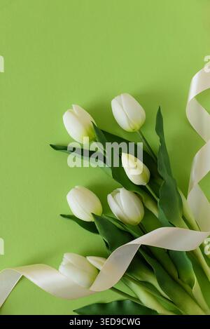 Elegant spring composition featuring white tulips arranged on a soft green background with a flowing satin ribbon. Easter or Mothers Day celebration Stock Photo