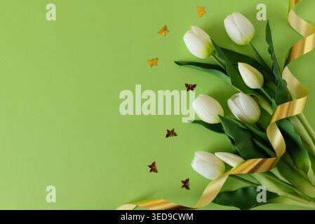 Elegant spring composition featuring white tulips arranged with butterflies confetti on a soft green background with a flowing satin ribbon. Easter or Stock Photo