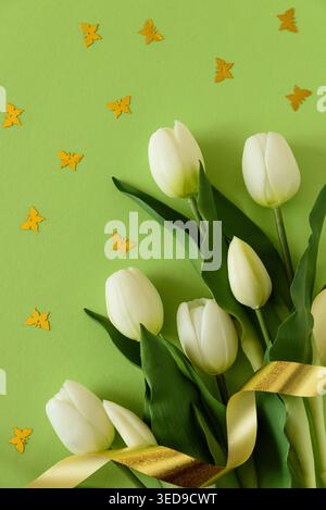 Elegant spring composition featuring white tulips arranged with butterflies confetti on a soft green background with a flowing satin ribbon. Easter or Stock Photo