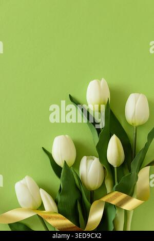 Elegant spring composition featuring white tulips arranged on a soft green background with a flowing satin ribbon. Easter or Mothers Day celebration Stock Photo