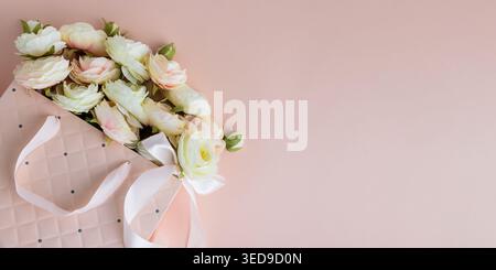 Festive composition featuring a quilted pink gift bag filled with cream and blush artificial rose flowers, accented by a white ribbon bow. Stock Photo