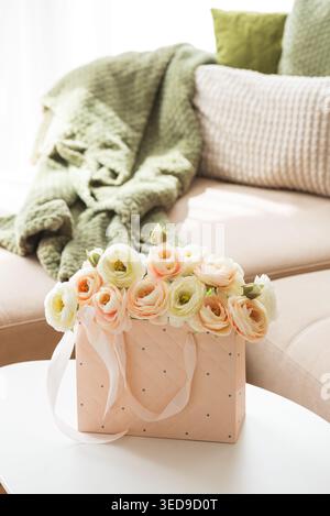 Delicate lifestyle composition featuring a quilted pink gift bag filled with cream and blush ranunculus flowers, accented by ribbon handles and decora Stock Photo