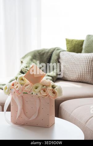 Delicate lifestyle composition featuring a quilted pink gift bag filled with cream and blush ranunculus flowers, accented by ribbon handles and decora Stock Photo