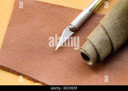 Precision Craft Knife with Brown Leather Sheet and Rolled Green Leather Piece on Amber Background Stock Photo