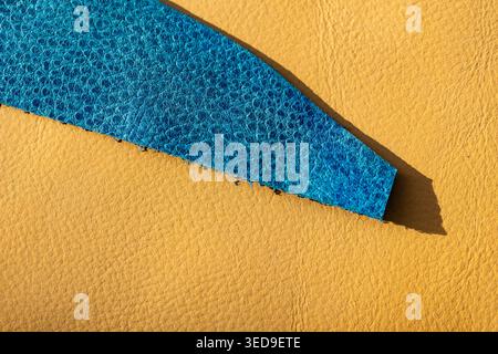 Iridescent Blue Leather Strip on Yellow Leather Surface with Natural Shadow, Exotic Craft Material Close-Up" Stock Photo