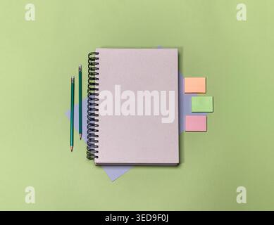 A blank notebook sits on a green surface. There are colored pencils and sticky notes nearby. This setup is ready for writing or planning activities in Stock Photo
