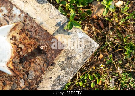 A close-up view of a rusty metal bolt on a weathered surface surrounded by green grass, highlighting the beauty of decay in natural environments. Stock Photo